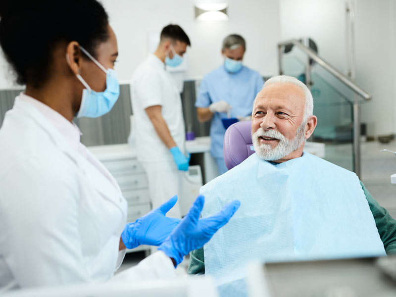 A mature man with a white beard smiling and talking to a dentist