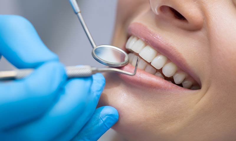 Dental assistand cleaning a womans healthy teeth with a small tool