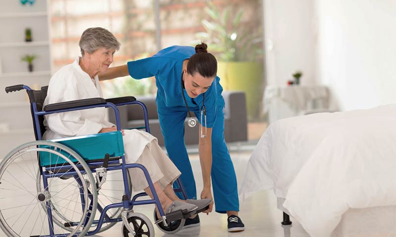 Nurse helping patient from wheelchair to bed