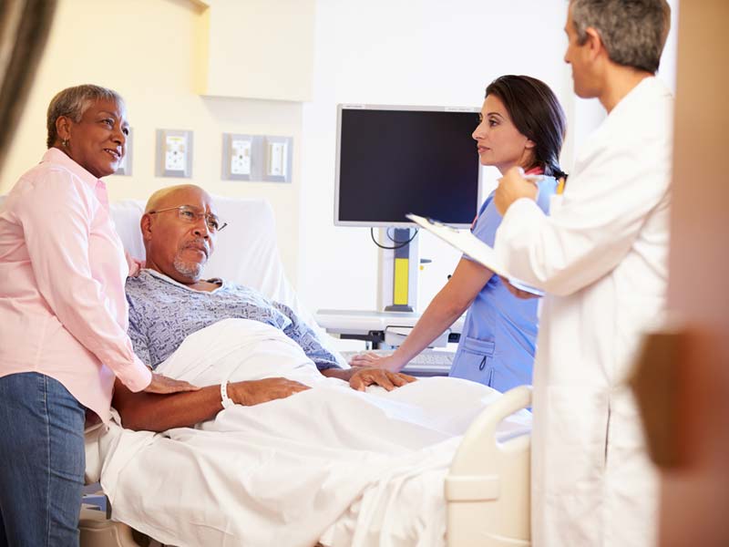 A senior man in a hospital bed with his wife talking to a doctor