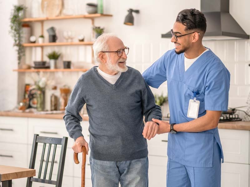 Senior man with a cane in his kitchen being assisted by a nurse